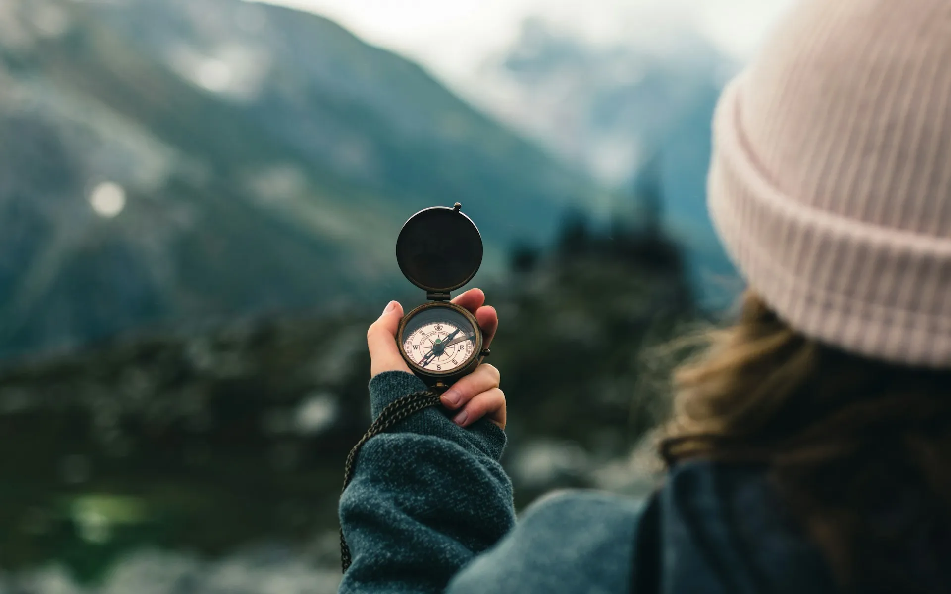 A person holds a compass up against a mountain in the background