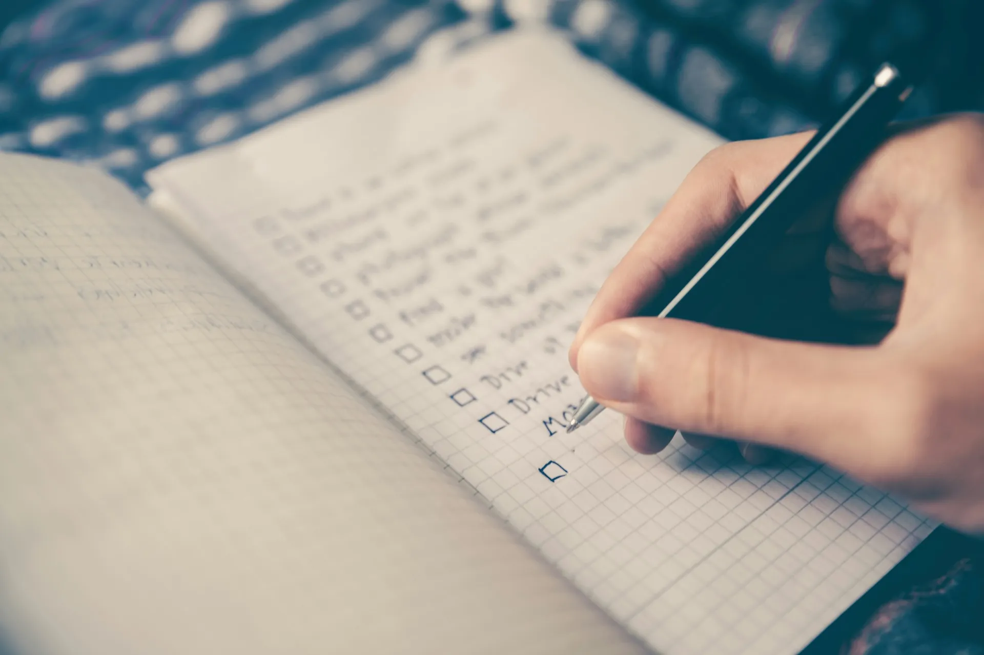 A person's hand writes out a checklist in a notebook